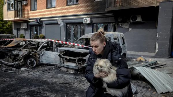 Жінка несе собаку біля зруйнованого будинку / Reuters